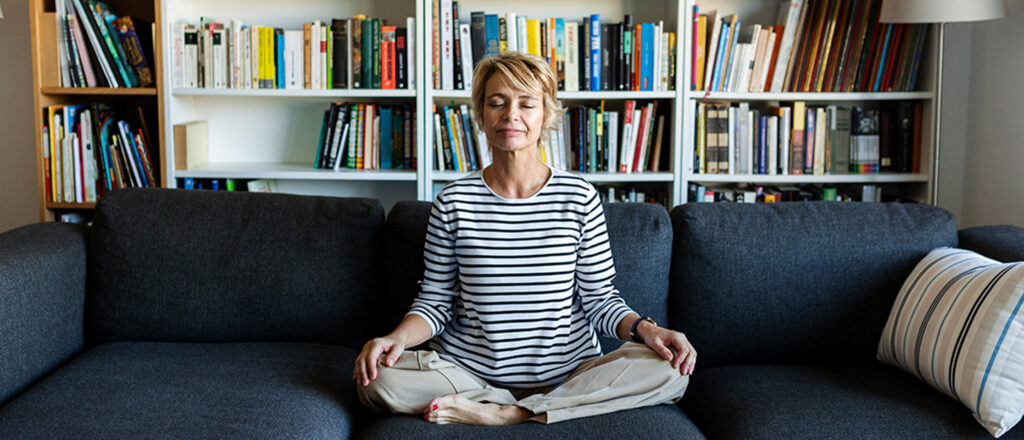 Woman sitting in a yoga pose with her eyes closed sitting on a couch in a home library
