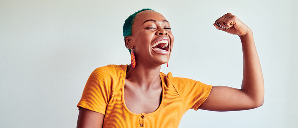 Young woman smiling flexing her left arm with an empowered expression