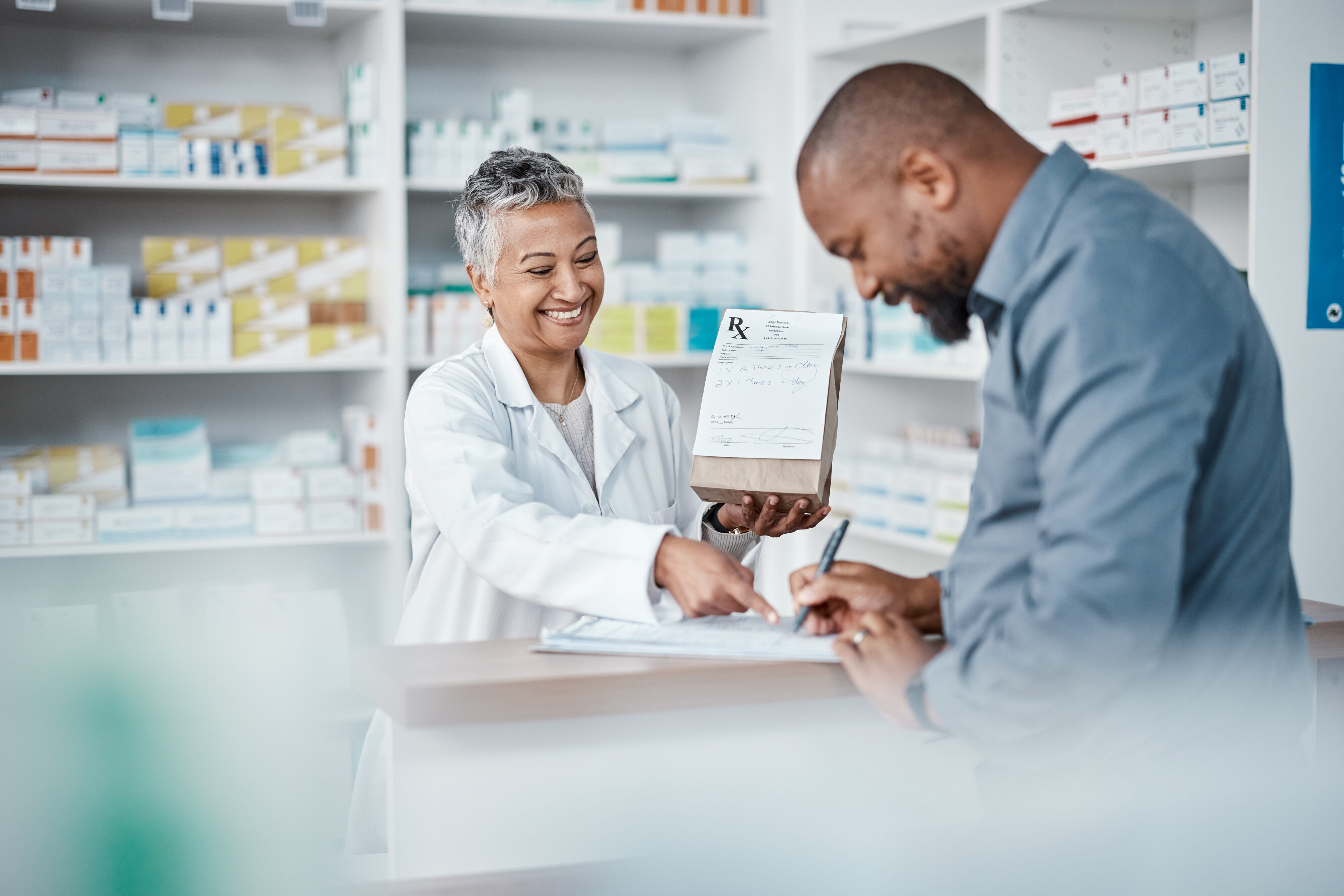 Man at pharmacy picking up prescription from woman pharmacist.