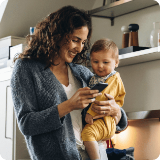 Young woman smiling holding her phone with one hand and her toddler with the other