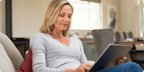 Adult woman sitting on a her couch reading on a tablet device